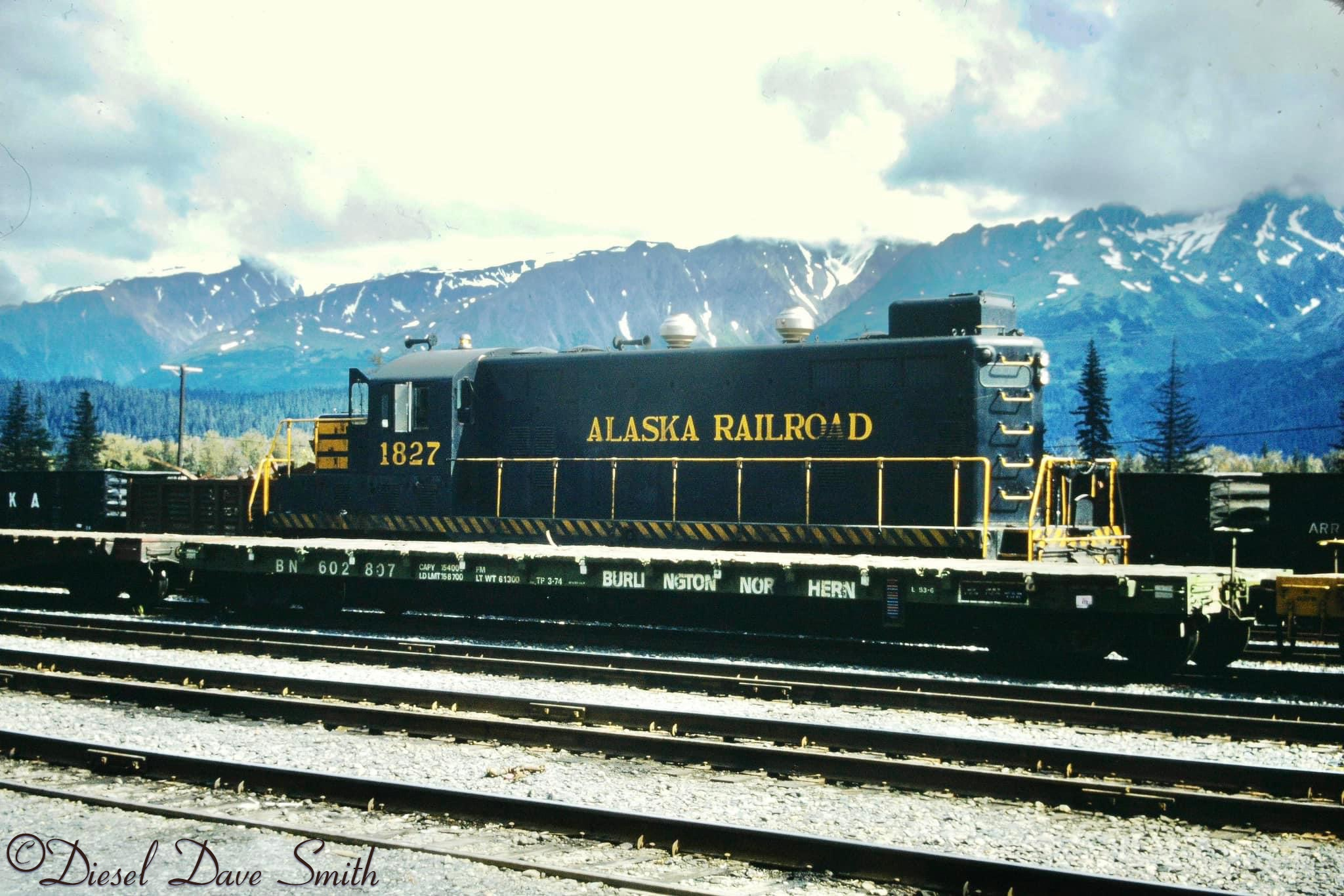 GP7L 1827 tries to hide behind a BN Flatcar in the yard at Seward. 8/11/75.